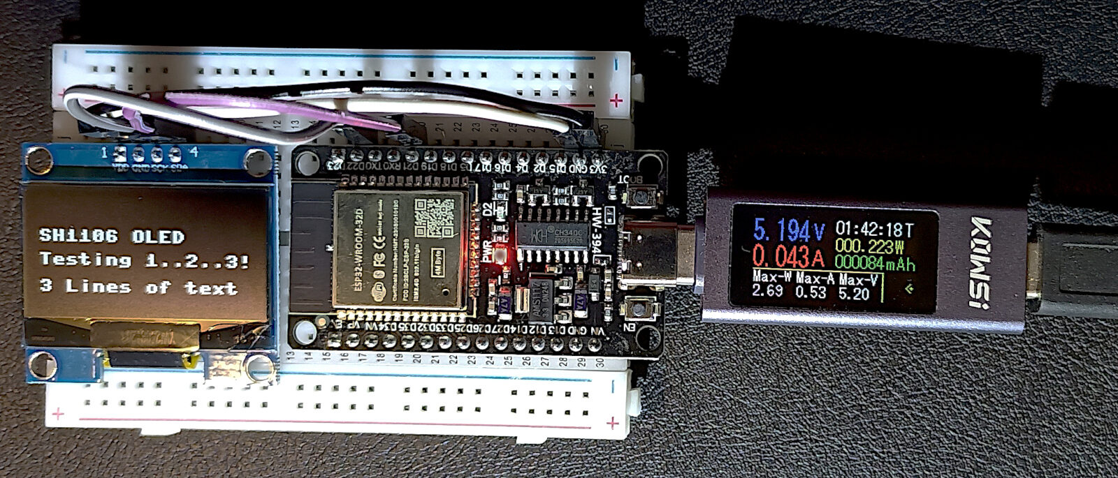 ESP32 board with an OLED display on a breadboard, powered through a USB meter reading 5.19 V and 0.043 A